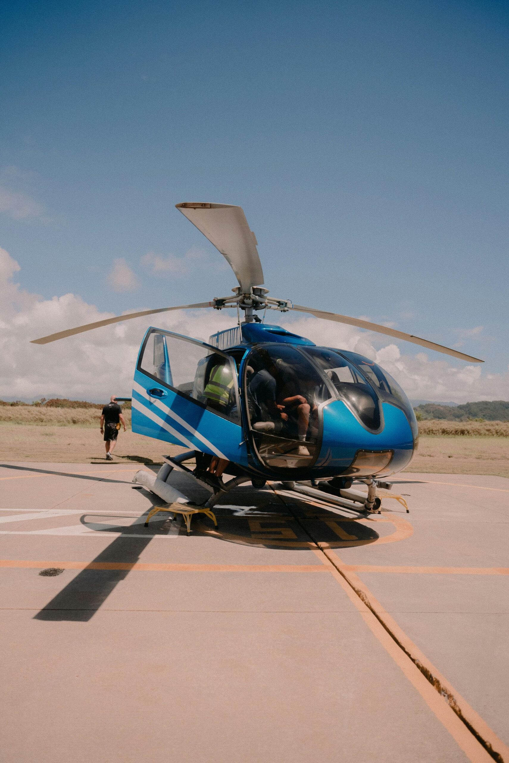 A blue helicopter stationed on a helipad under a clear blue sky.