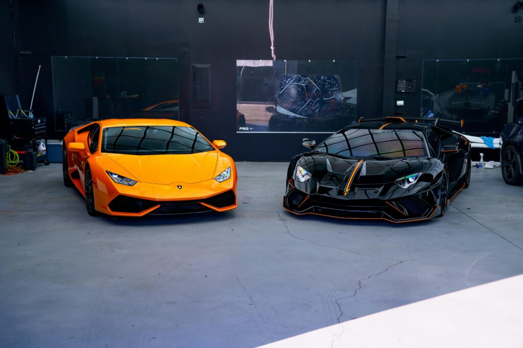 Two luxury sports cars, orange and black, parked in a stylish indoor garage.