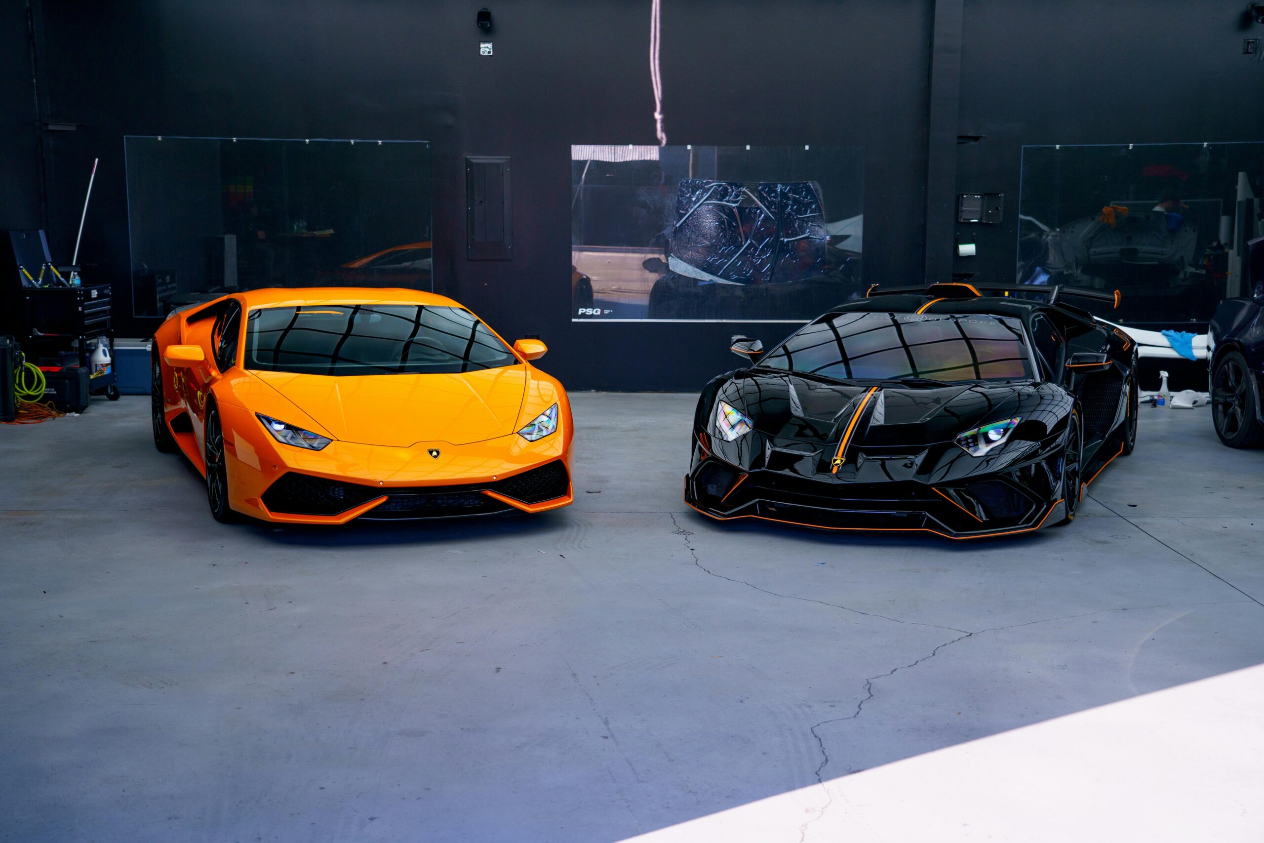 Two luxury sports cars, orange and black, parked in a stylish indoor garage.