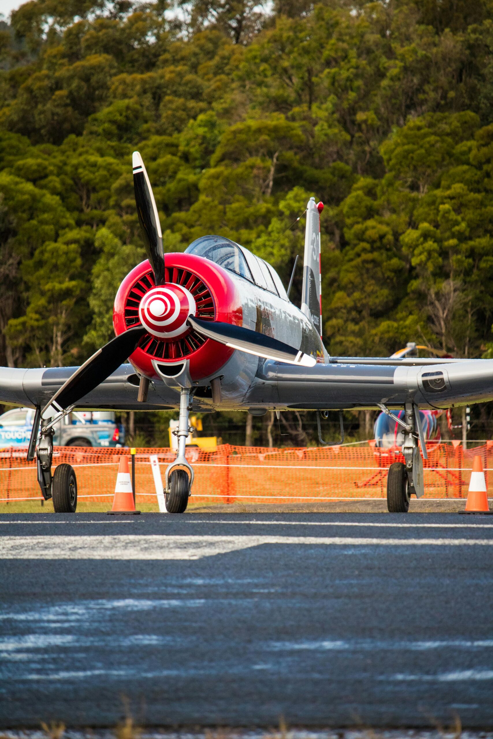 Front view of a vibrant propeller plane parked on a runway surrounded by greenery.